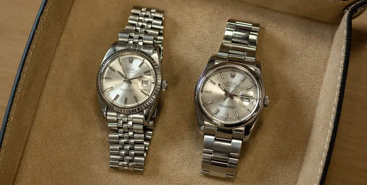 Two silver Rolex Datejust watches with metal bands displayed in a tan suede-lined watch box.