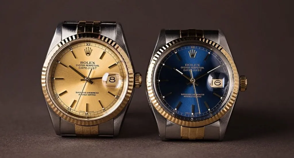 Side-by-side close-up of Rolex Datejust watches model 16233 with gold dial and 16013 with blue dial on a dark background.