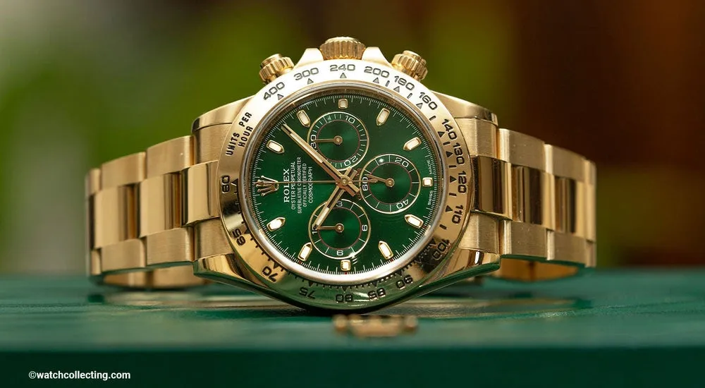 Close-up of a gold Rolex Daytona watch with a green dial and chronograph features on a green surface.