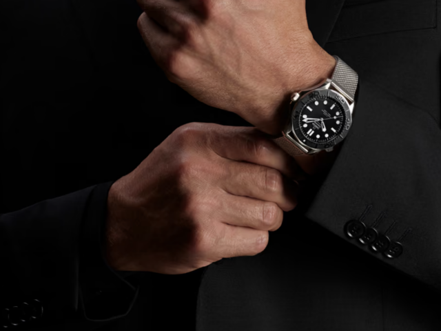 Man in a dark suit wearing the Omega Seamaster Diver 300M Spectre Edition on a steel mesh bracelet